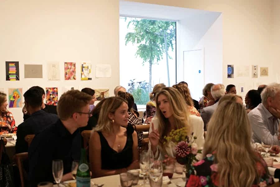 A group of people sat along trestle tables in a gallery space